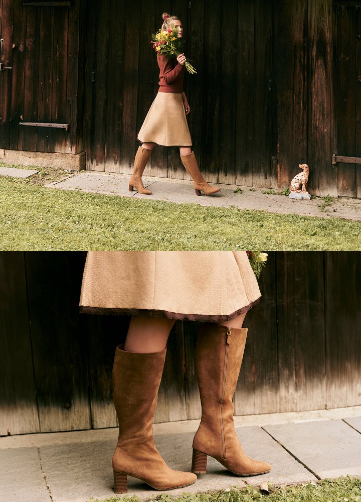 A split two-panel lifestyle photograph showcasing a pair of mid-calf brown suede boots. The top panel shows a woman from the waist down walking past a dark wooden barn wall while holding a bouquet of flowers, and the bottom panel is a close-up of the boots on a stone path in front of the same wooden wall.
