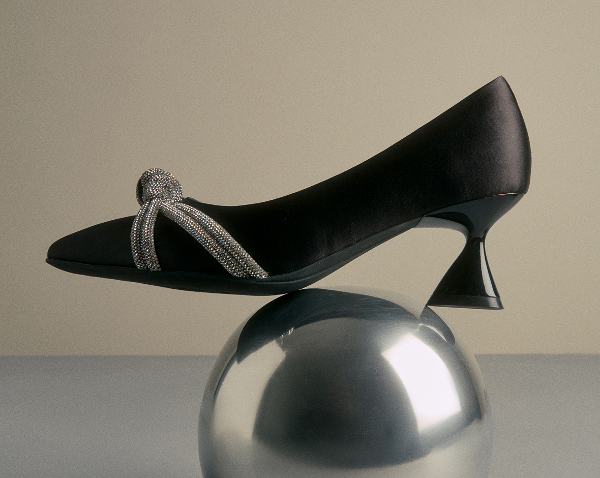 Black shoe with decorative bow on a reflective surface
