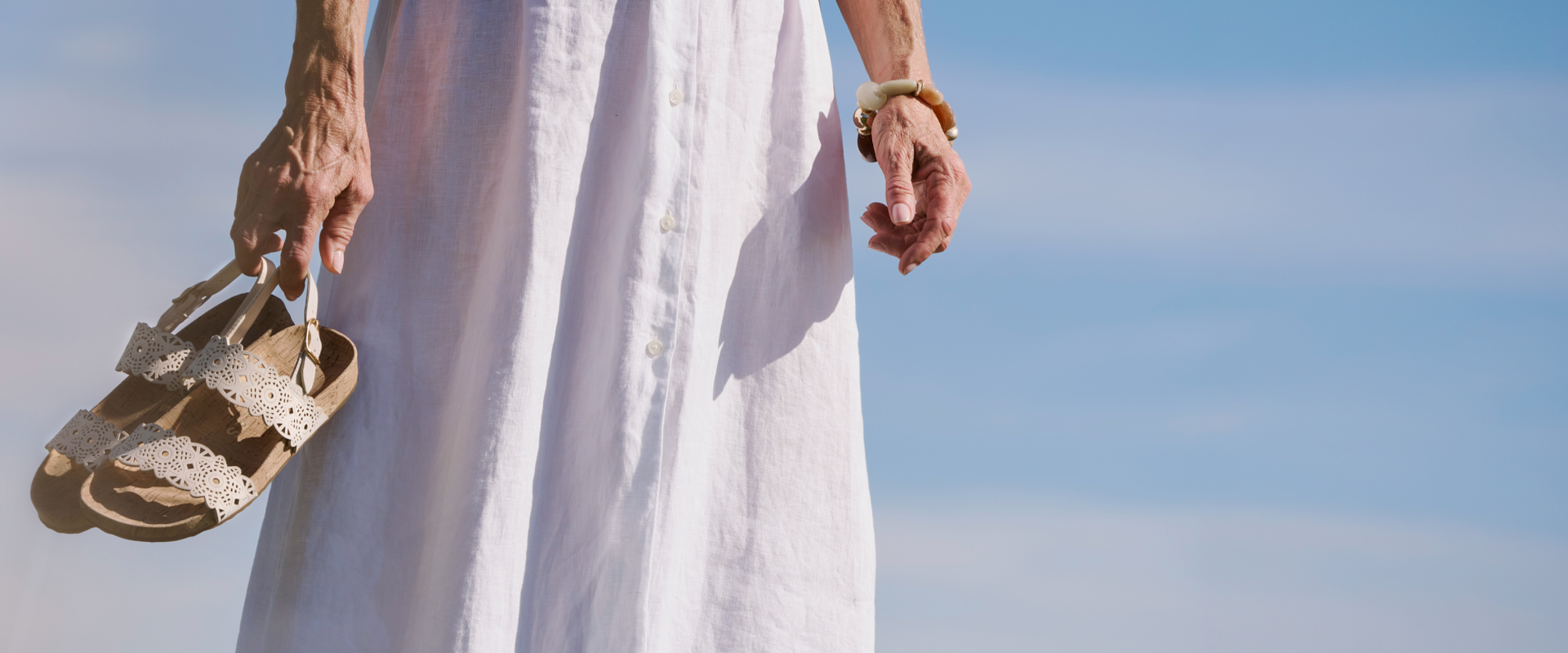 Person wearing a white dress holding sandals against a clear blue sky. buy one full-price item, get an extra 30% off one sale item