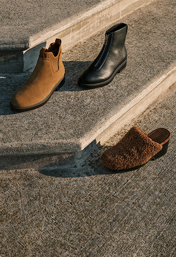 Two pair of boots and one heeled mule on a concrete surface with a step.