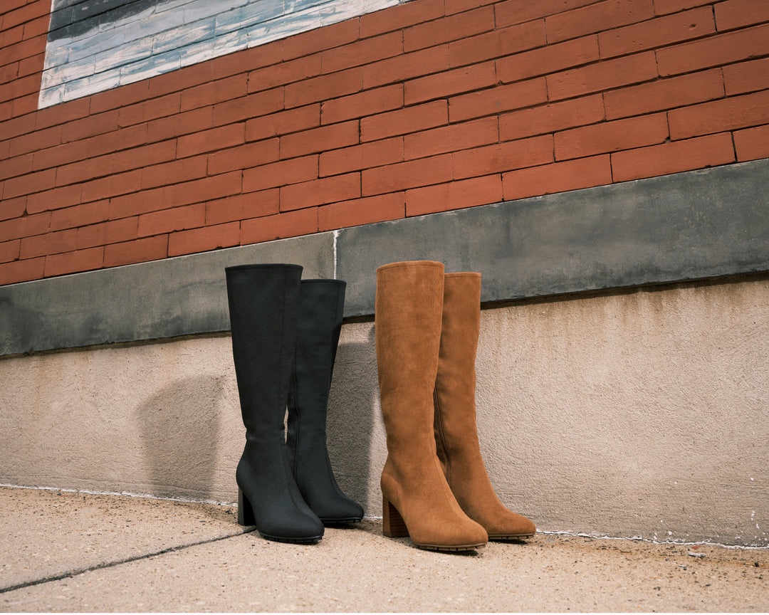 Black and brown knee-high boots leaning against a brick wall.