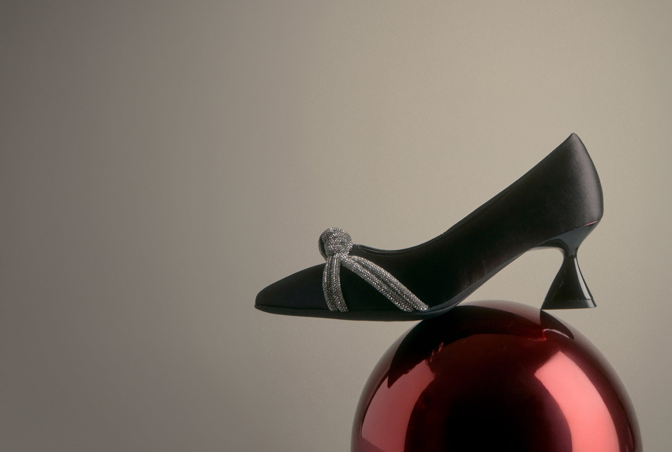 Black high-heeled shoe with a decorative bow on a reflective red surface against a beige background. the holiday shop. 