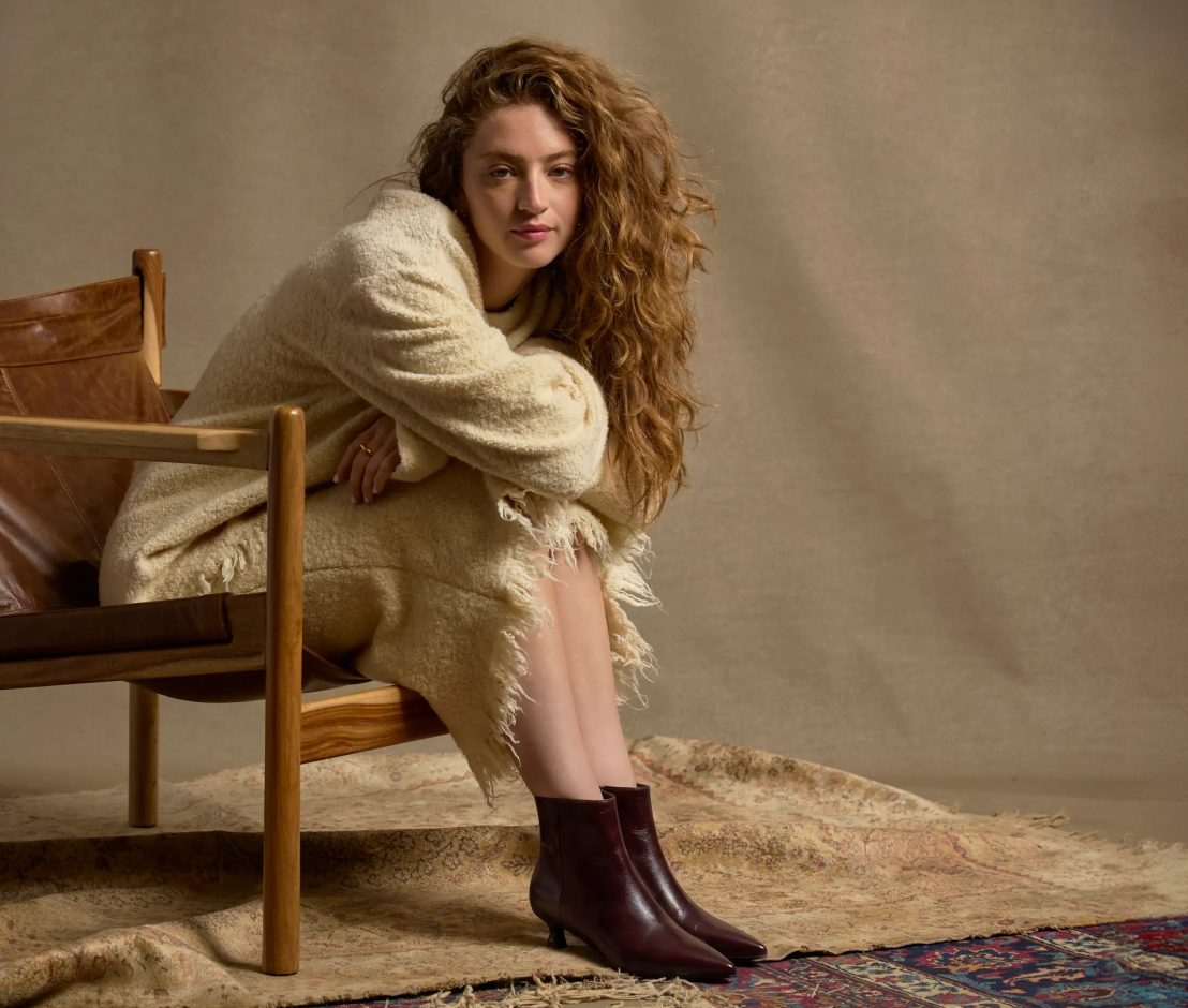 woman sitting on chair wearing cream outfit and burgundy ankle boots