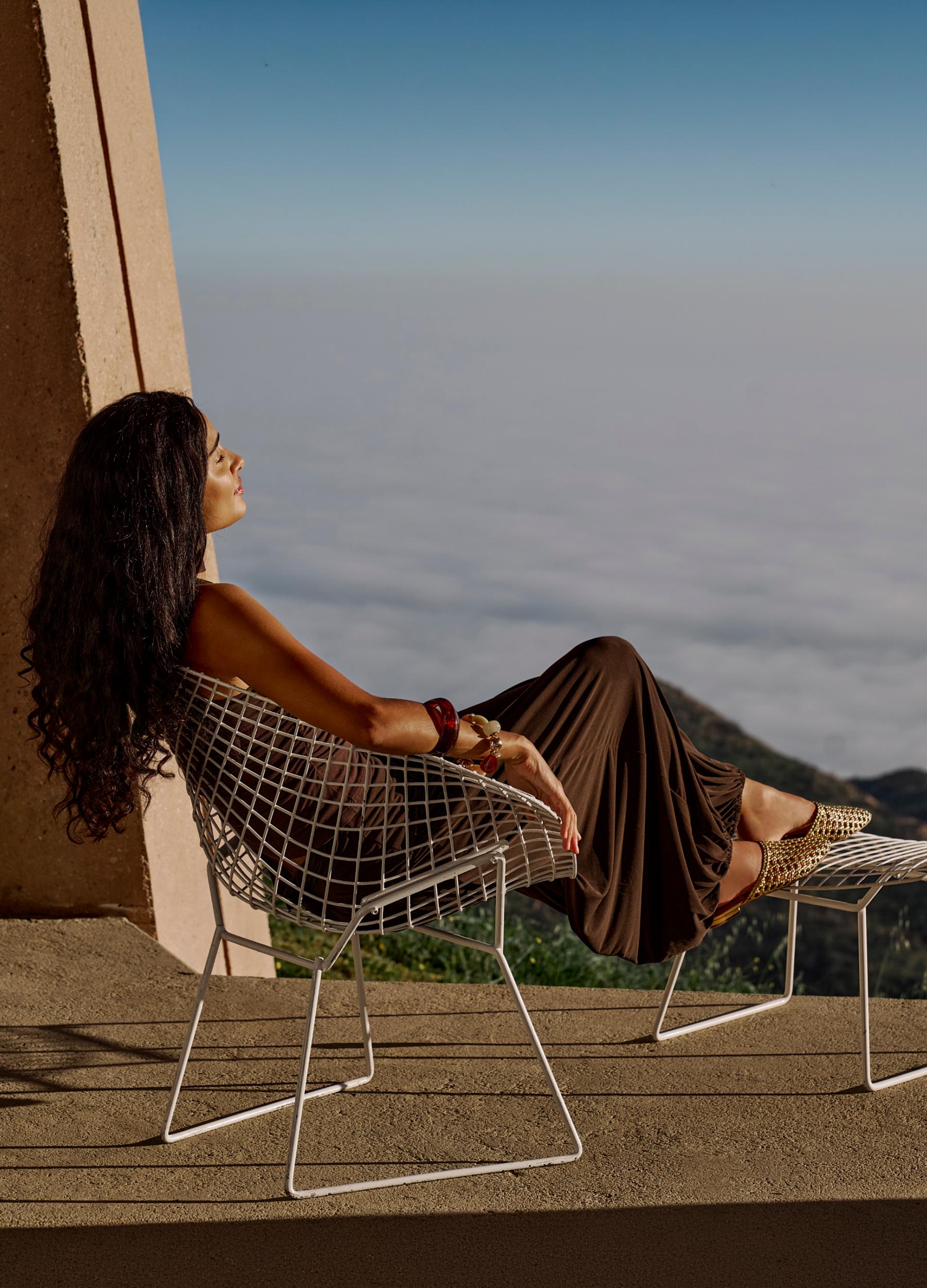 Made to Get Away. The newest arrivals, made for exploring in style. Woman sitting on a metal chair with a scenic view of mountains and clouds.
