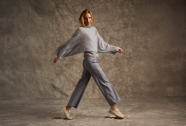 Woman in a gray sweater and pants posing against a textured brown background