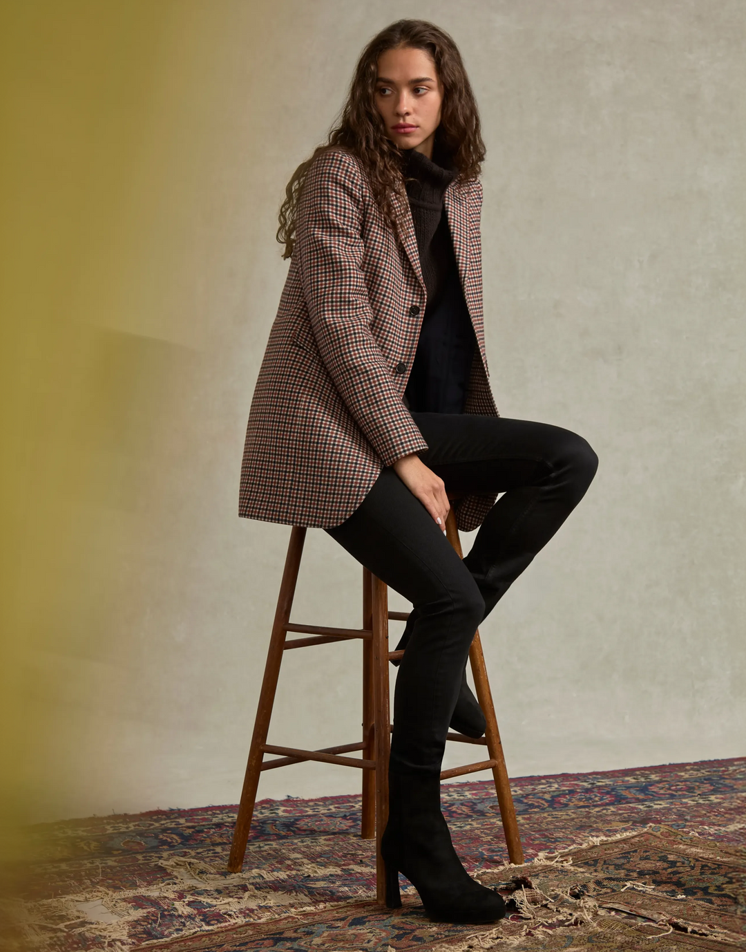 woman sitting on stool in studio wearing a blazer and heeled booties