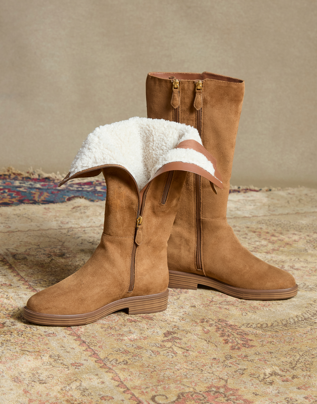 still shot of tobacco faux suede boots. one boot is unzipped to show the shearling lining. 