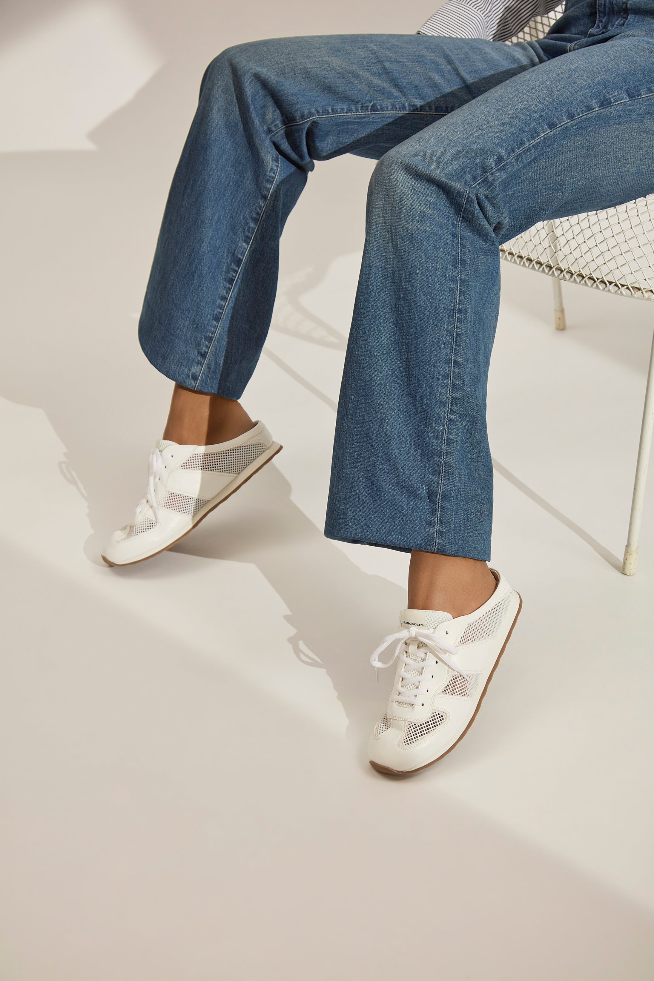 Person wearing blue jeans and white sneakers on a light background