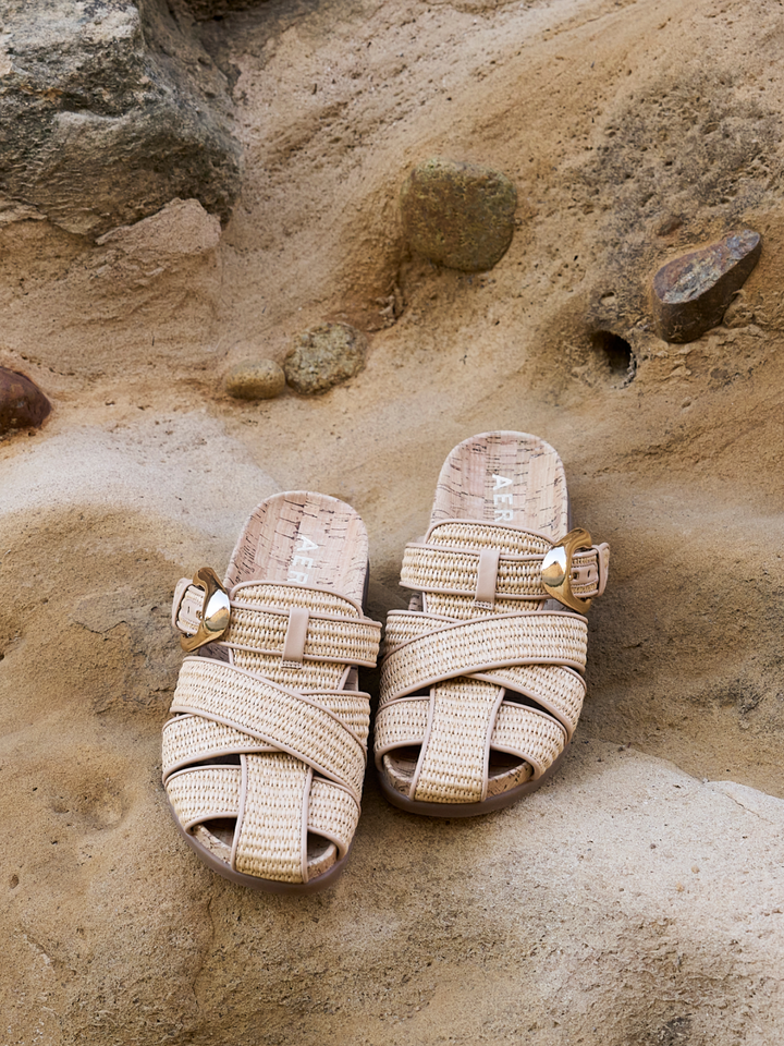 Pair of woven sandals with gold accents on a stone surface