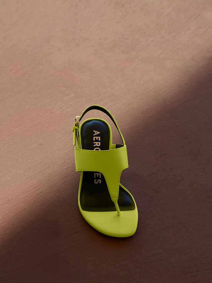 Lime green sandal with black sole on a brown background