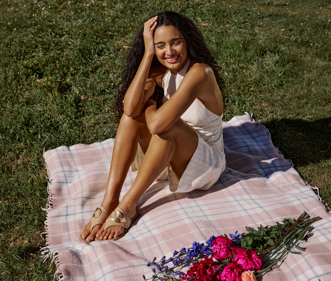 Woman sitting on a plaid blanket with flowers in a grassy field
